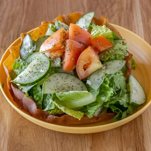 A vibrant Mediterranean salad with lettuce, cucumbers, and tomatoes in a crispy pita bowl.
